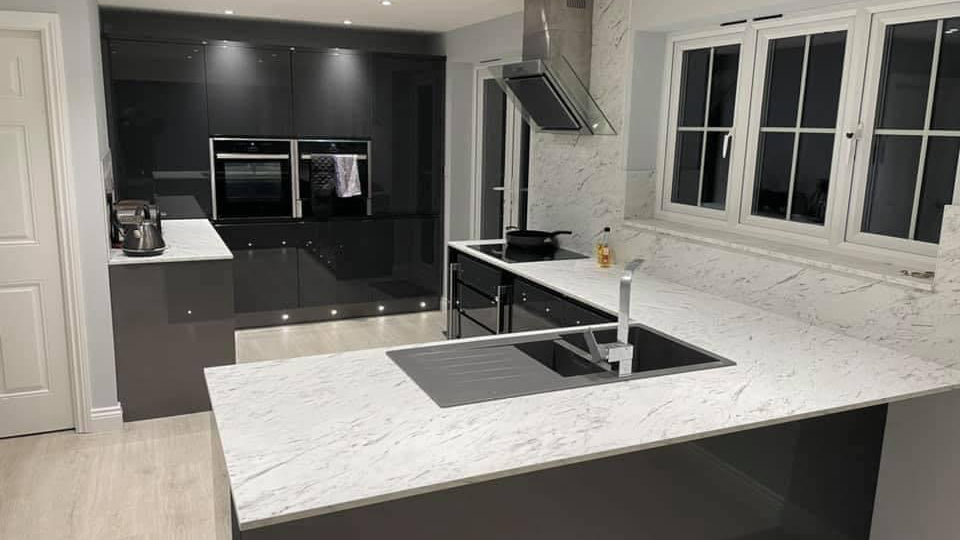 Dark grey gloss handleless kitchen with a white marble-effect worktop and plinth lighting
