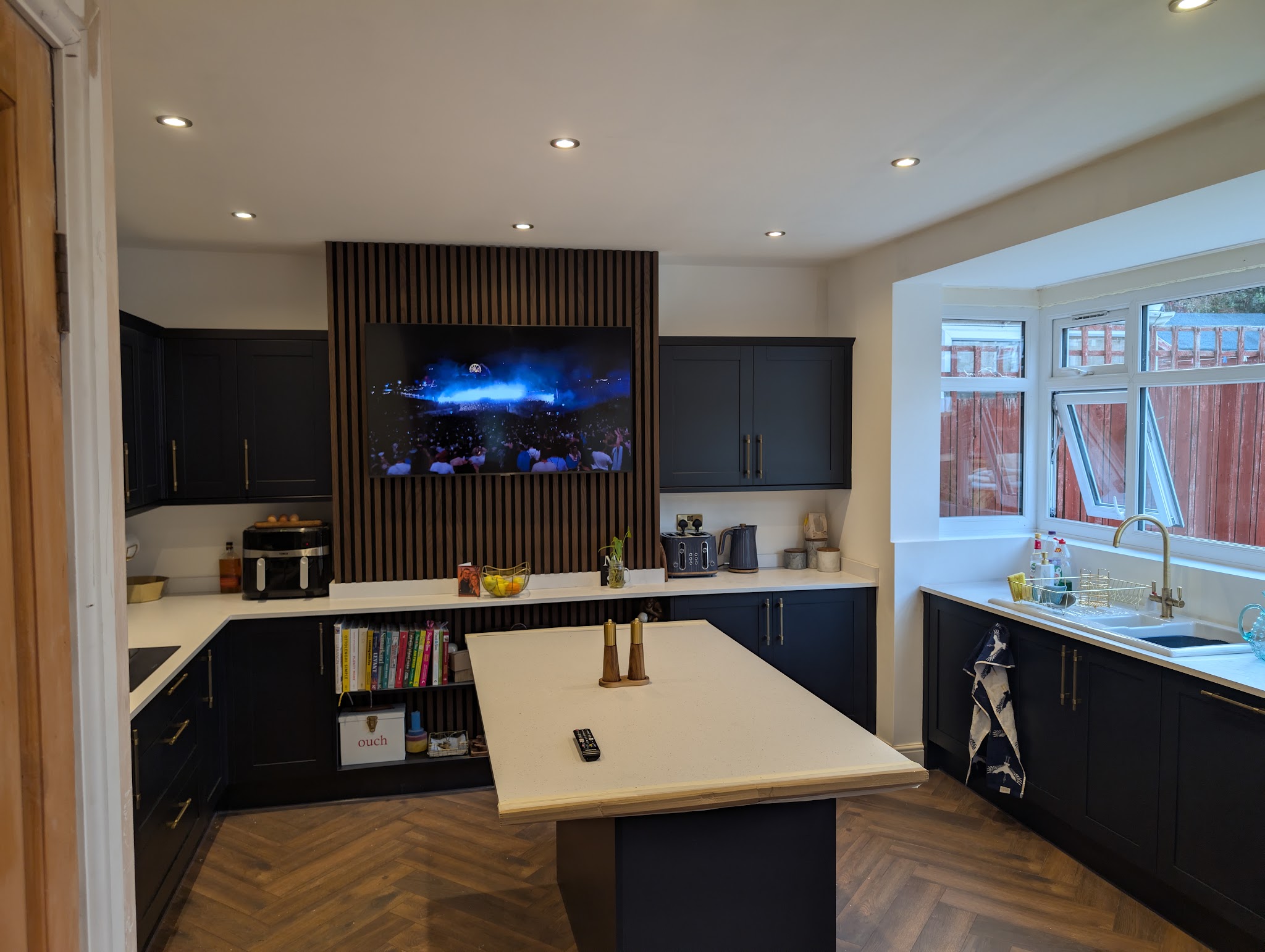 Navy kitchen with an island, herringbone floor and a slatted timber media wall