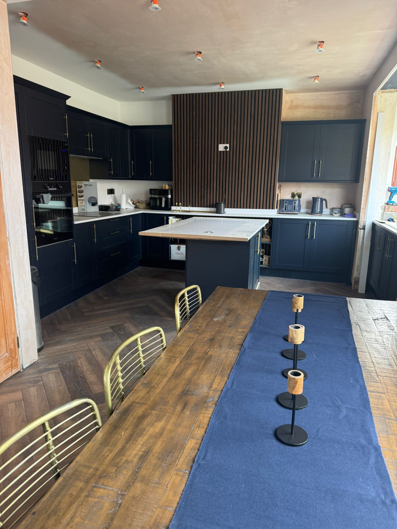 View down a kitchen diner: navy units, an island and a long timber dining table